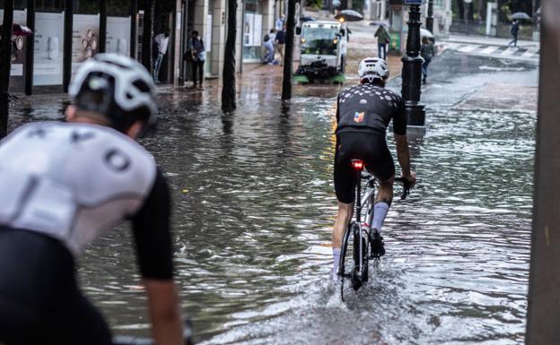 Dos ciclistas circulando por el centro de Oviedo. En el vídeo, algunas zonas de la capital anegadas.