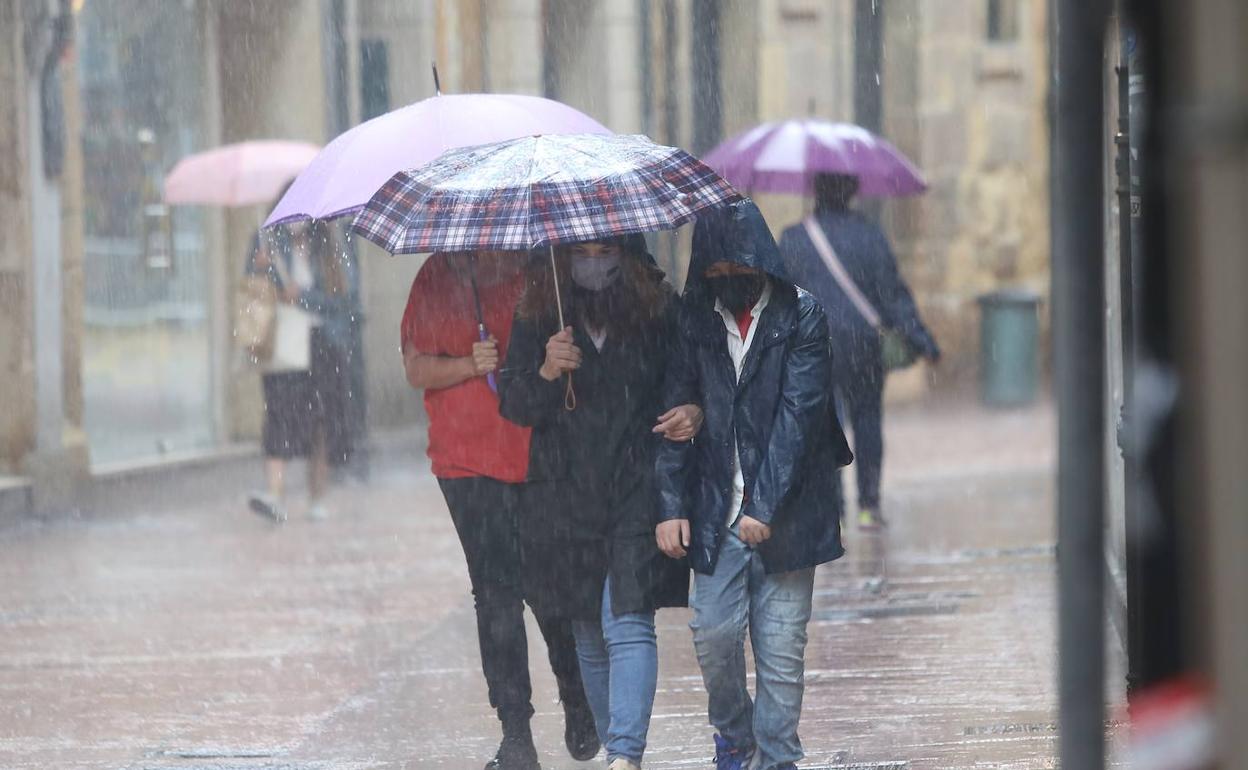 Paseantes por el centro de Oviedo se protegen de la lluvia con un paraguas. 