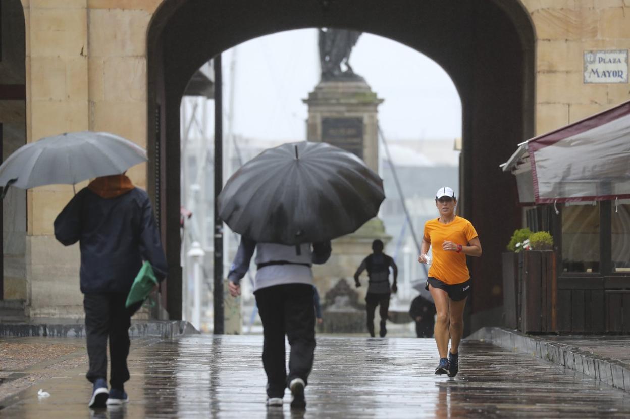 Varios gijoneses pasean y corren bajo la lluvia. 