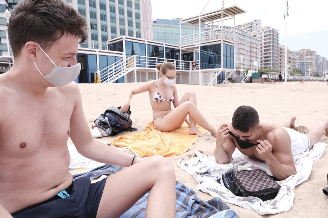 Unos jóvenes se ponen la mascarilla en la playa de San Lorenzo. 