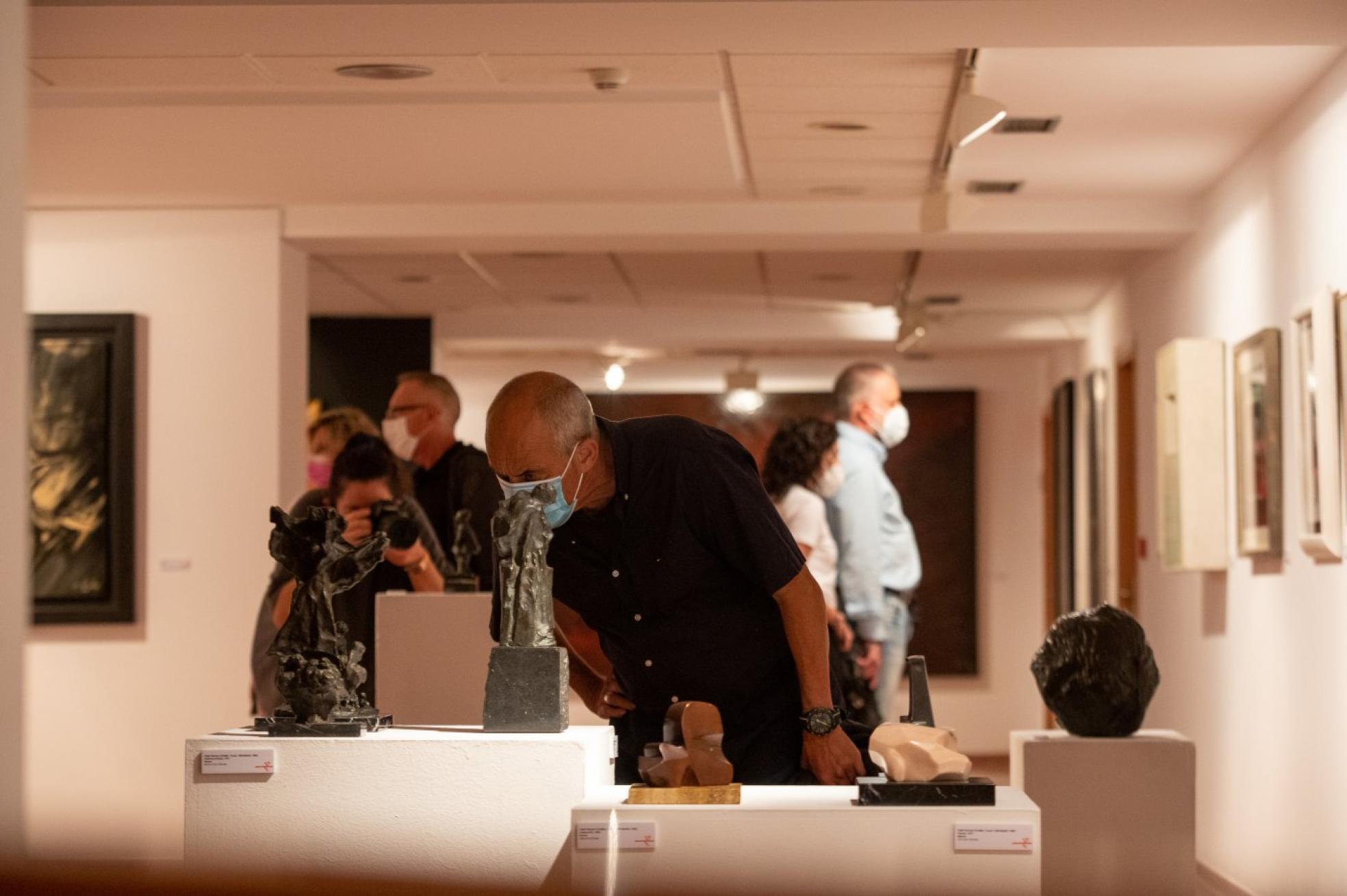 Un visitante observa con atención las esculturas de Pablo Serrano en el Centro Municipal de Arte y Exposiciones de El Arbolón. Uno de los cuadros, firmado por Antonio Suárez antes de 1955, en el que se aprecia un estilo más figurativo.