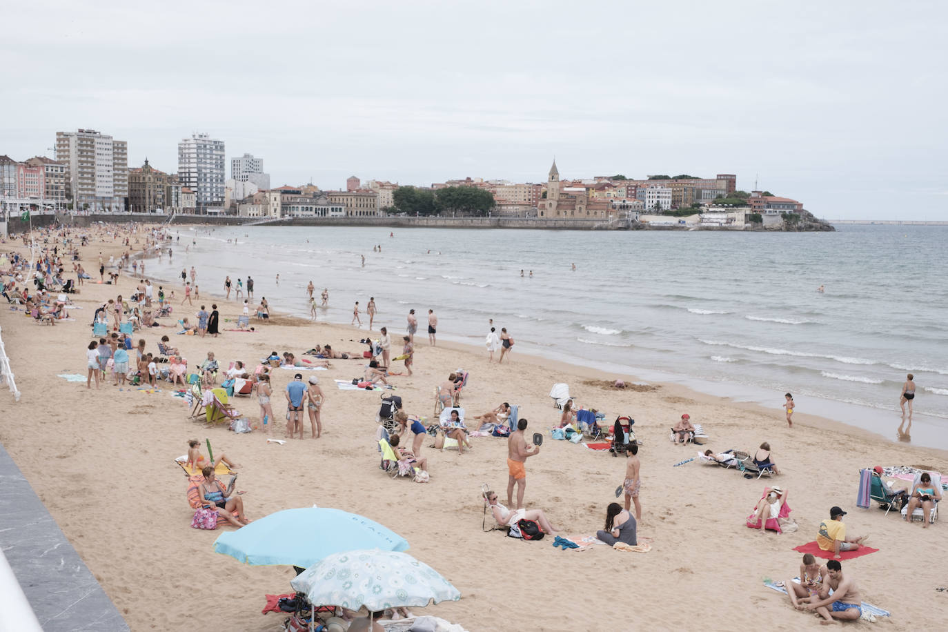 Está siendo un verano atípico en la costa asturiana, pero el mal tiempo no ha impedido que los bañistas se lancen a la playa de San Lorenzo con ganas de disfrutar del día. Algunos pasean, otros leen con la ropa puesta y los más valientes se atreven a darse un chapuzón. Cualquier plan es preferible a quedarse en casa.