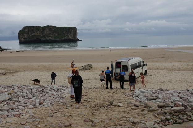 Los agentes de policía conversan con los dueños de la furgoneta atascada en la playa de Andrín. 