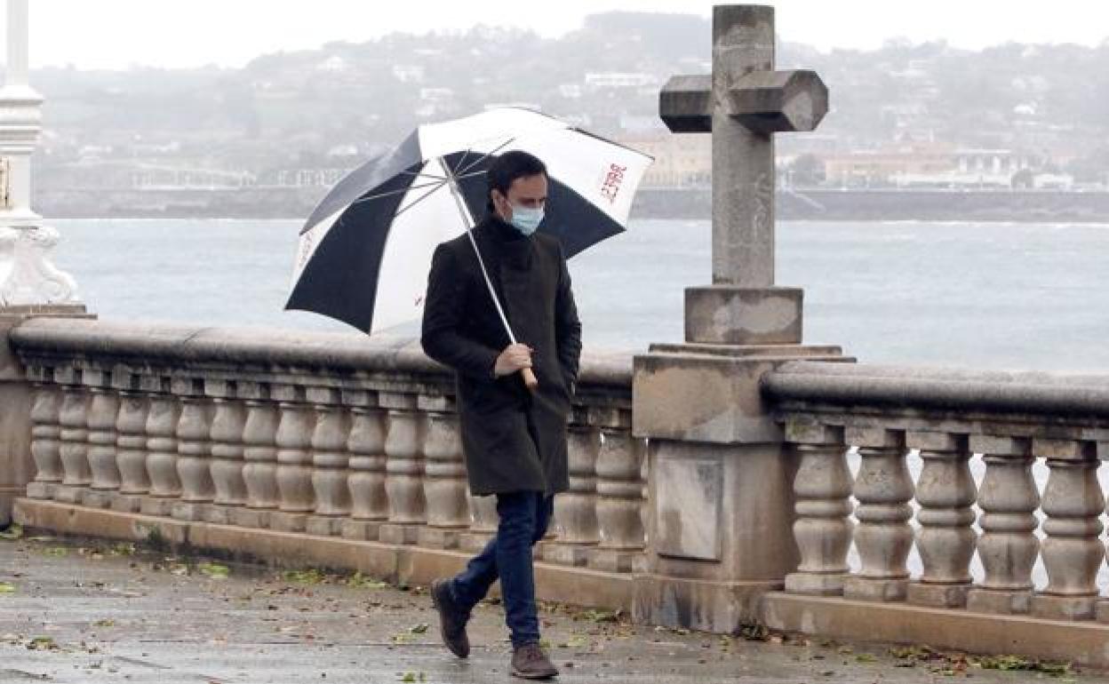 Una persona pasea bajo la lluvia en Gijón.