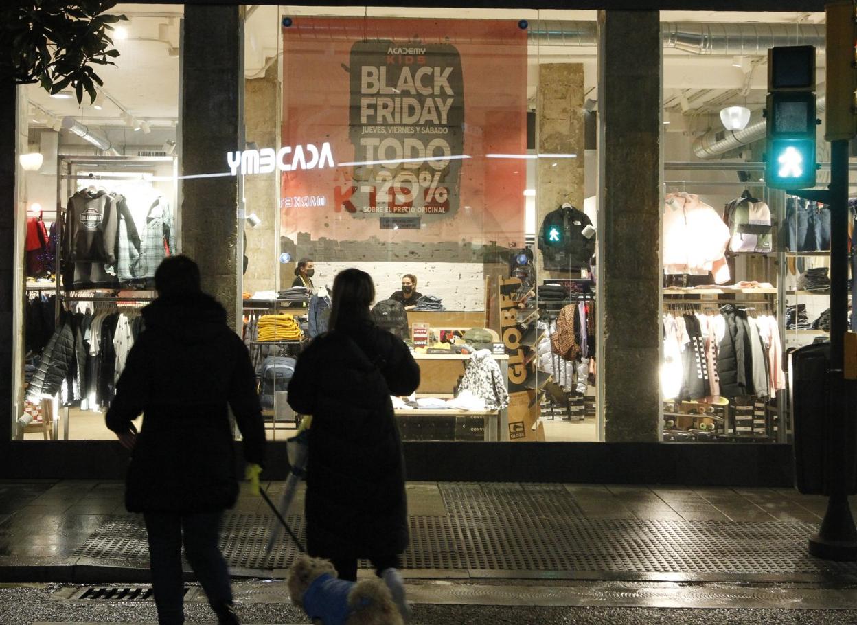 Dos personas observan un escaparate en Gijón un cartel que anuncia rebajas por el 'Black Friday'. 