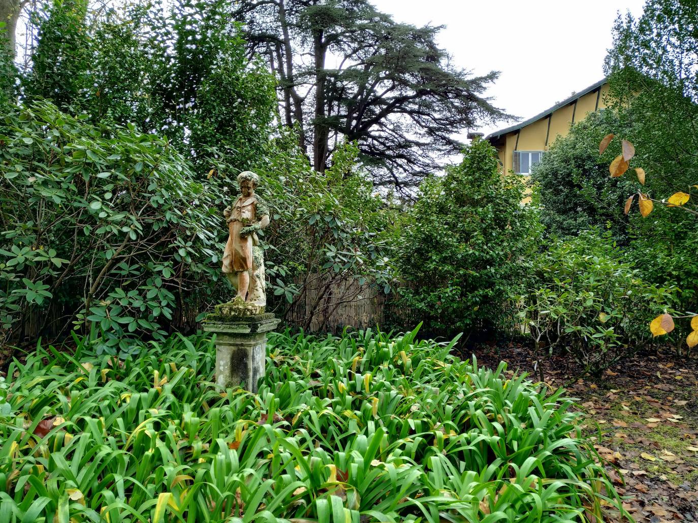 Rincón de agapantos y rosales ante 'la mesona', con una escultura clasicista de piedra (anterior al siglo XIX)y la casa al fondo 