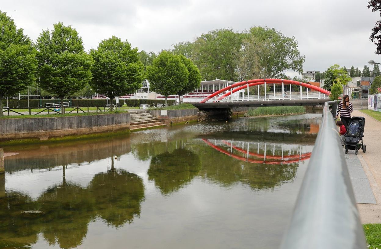 Una mujer camina por la senda anexa al Piles a su paso junto a las instalaciones deportivas de Las Mestas. 