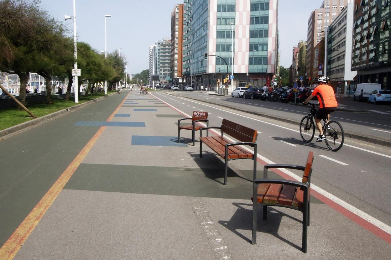 Un ciclista circula por el carril bici al lado de tres bancos del 'cascayu', que forman parte del mobiliario que será retirado el lunes.