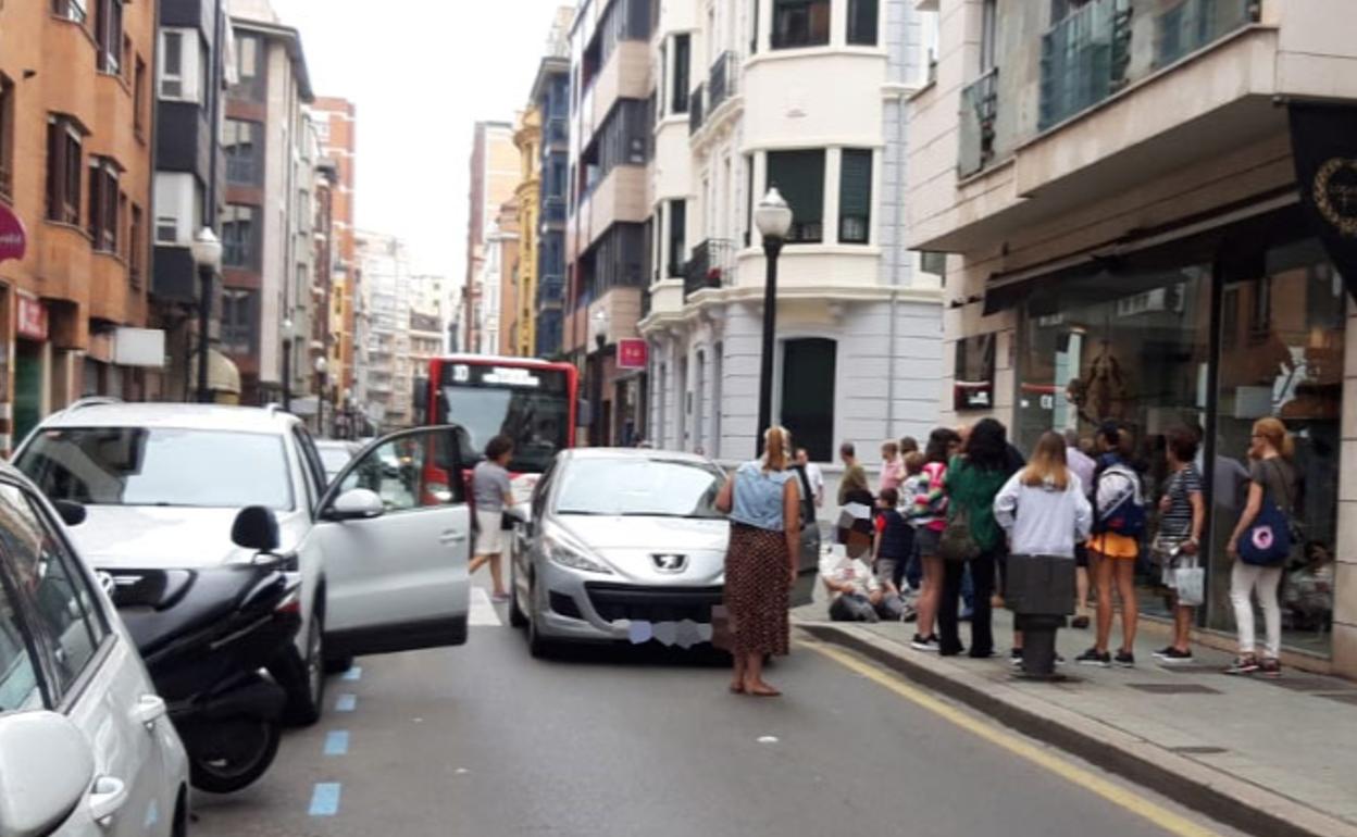 El vehículo implicado en el accidente; el herido, en la acera, asistido por un grupo de viandantes.