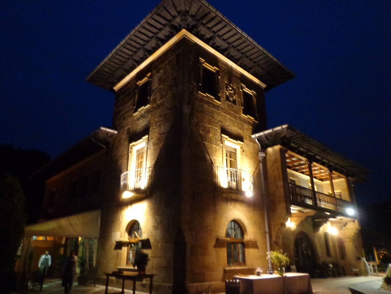 Escudo de armas de los Bernaldo de Quirós en el centro de la torre, en una espectacular fotografía nocturna con el palacio iluminado.