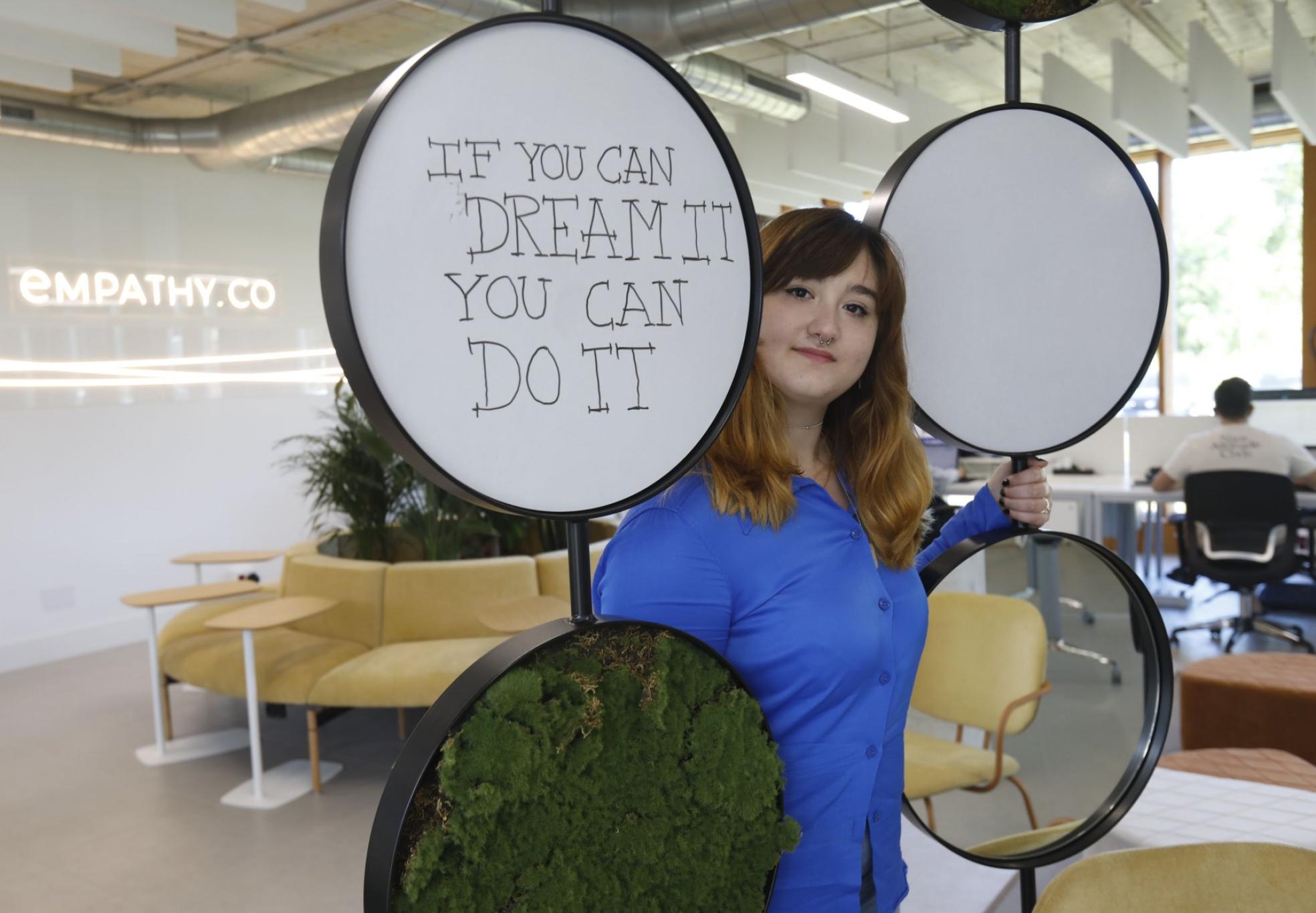 La informática Ana María García posa en Empathy, la empresa donde trabaja, con un cartel que dice 'Si puedes soñarlo, puedes hacerlo'. 