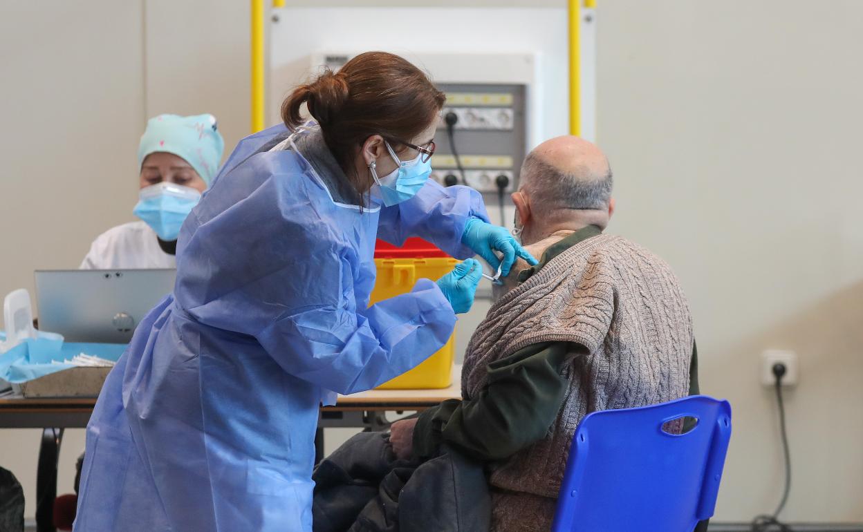 Una sanitaria inyecta una vacuna a un hombre mayor.