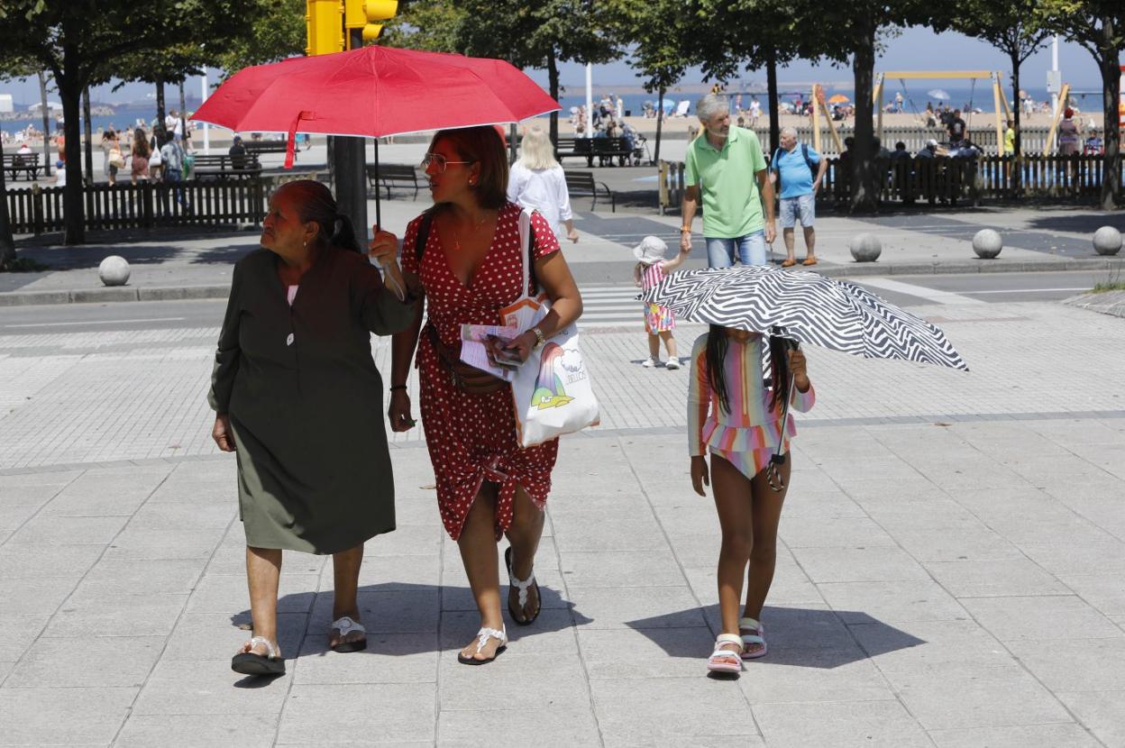 Dos mujeres y una niña se protegen del sol con paraguas en su paseo por las inmediaciones de la playa de Poniente. 