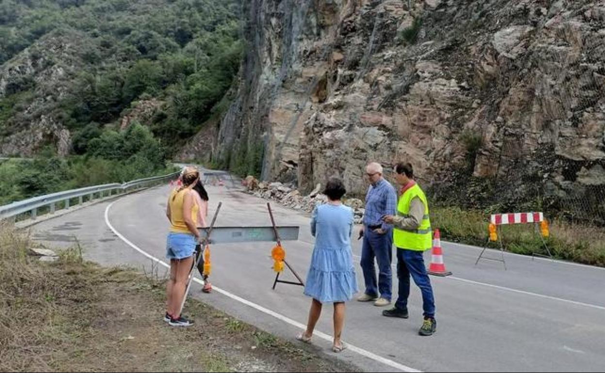 Varias personas observan las rocas retiradas a un lado de la carretera. 