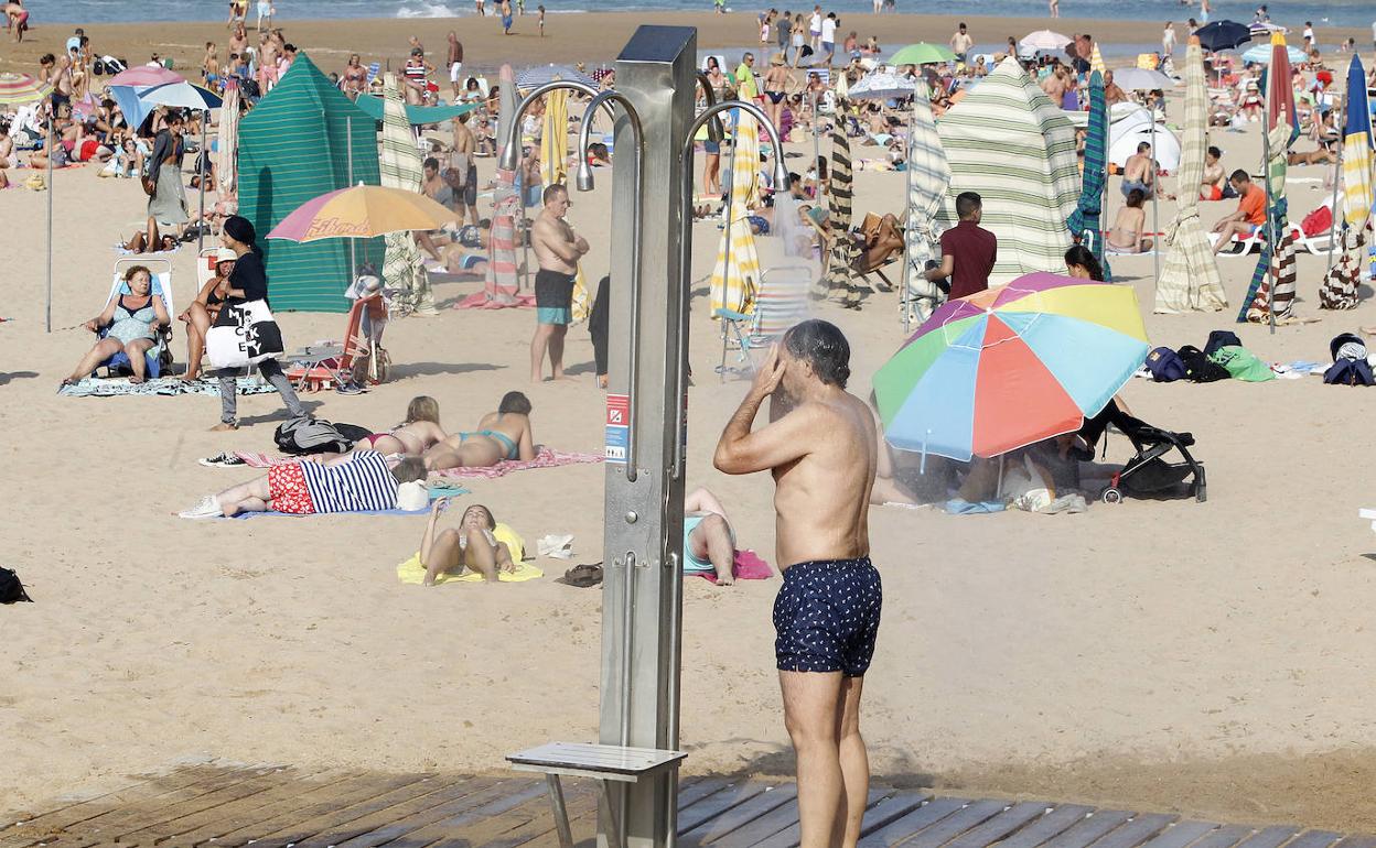 Un hombre se refresca en una de las duchas de la playa de San Lorenzo. 