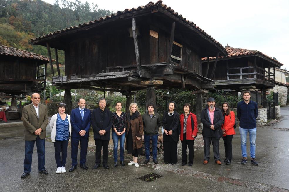 Shigeru Ban y su esposa Masako -ambos vestidos de negro-, junto al alcalde de Ribera de Arriba, Tomás Manuel Fernández (a la izquierda del arquitecto), el director del centro de interpretación, Roberto Álvarez, y un grupo de vecinos de Bueño, ante tres hórreos centenarios. 