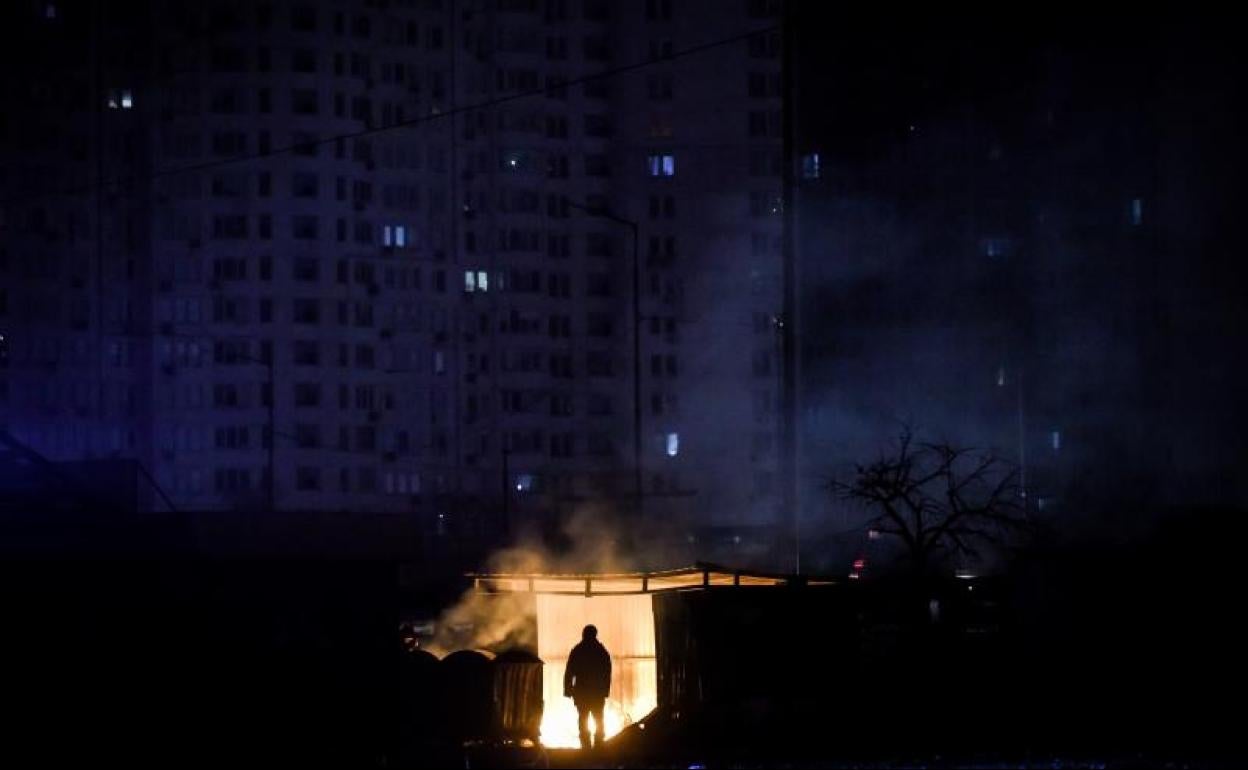 Un hombre se calienta en una hoguera junto a un edificio sin suministro eléctrico en Kiev. 