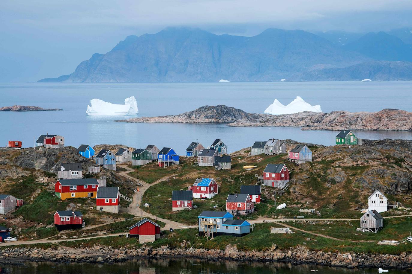 Una fotografía tomada el 19 de agosto de 2019 muestra icebergs flotando cerca de la costa detrás de casas coloridas en Kulusuk (también escrito Qulusuk), un asentamiento en el municipio de Sermersooq ubicado en la isla de mismo nombre en la costa sureste de Groenlandia.