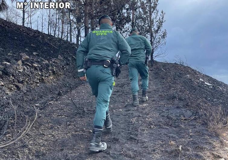 Dos agentes de la Guardia Civil rastrean una de las zonas calcinadas por los incendios.