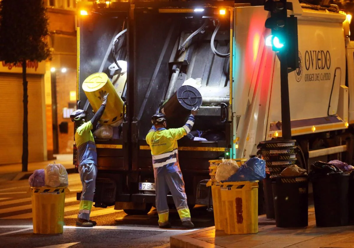 Dos operarios recogen los cubos y tiran los residuos en los compartimentos del camión en una calle.