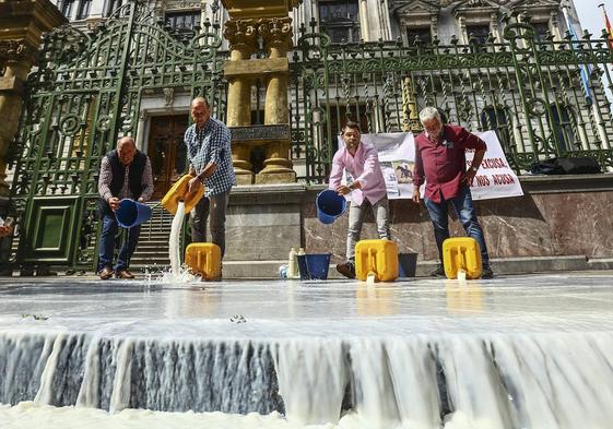 Representantes del sector ganadero derraman leche a la entrada de la Junta General del Principado como protesta por la propuesta de bajada del precio por litro producido.