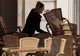 Una camarera colocando una silla en una terraza.