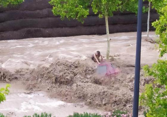 Una mujer se agarra fuertemente a su vehículo para no ser arrastrada por la riada.