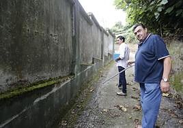 El presidente de la asociación vecinal Muselín Vivo, Sotero Rey (centro), muestran el arañazo de una UVI móvil que intentó pasar por el Camín Vieyu del Musel.