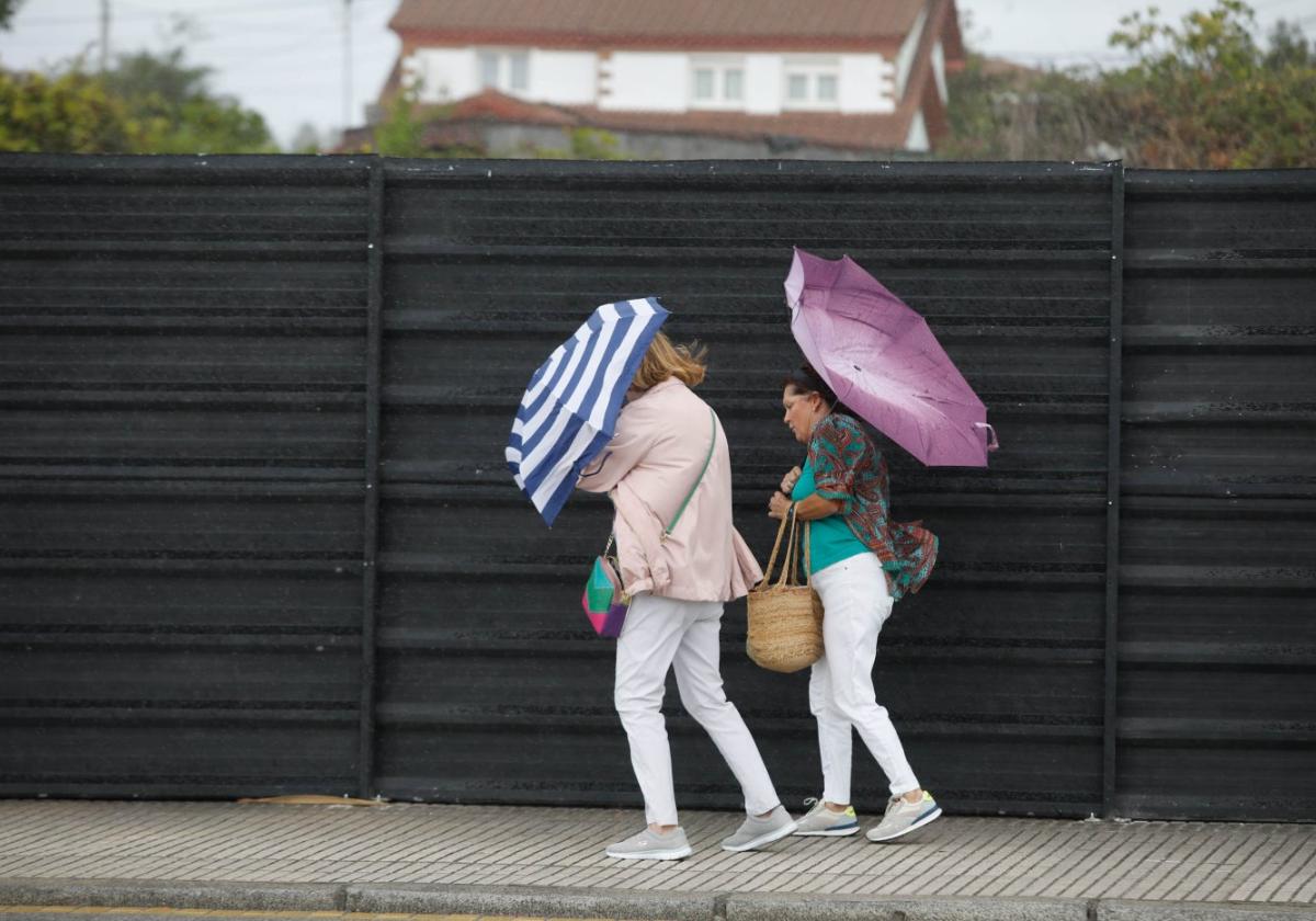 Unas mujeres tratan de resguardarse de la lluvia y el fuerte viento mientras caminan por una calle de Gijón.