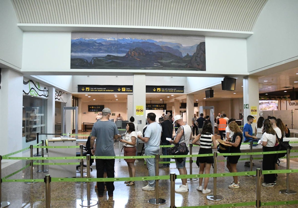 Pasajeros esperan su turno para pasar por los arcos de seguridad en el acceso a la zona de embarque del Aeropuerto de Asturias.