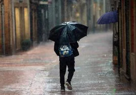 Un joven pasea por las calles mojadas de Oviedo con paraguas en mano.