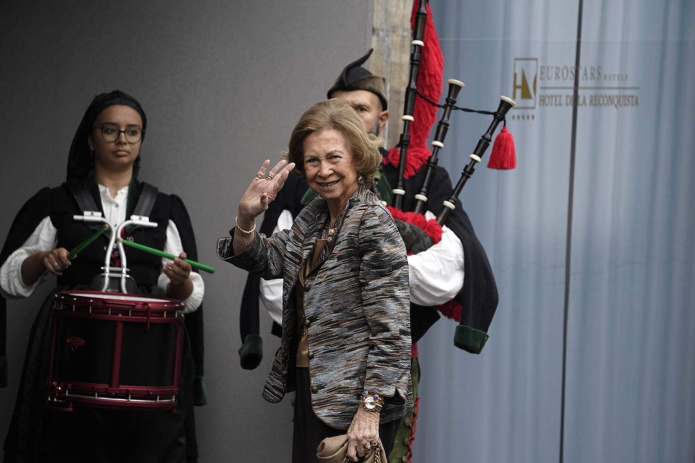 Fiel a su estilo, la reina emérita, doña Sofía, también ha optado por un dos piezas. Ha combinado una americana de tonos frises, negros y marrones con una camisa camel y un bolso del mismo color. 