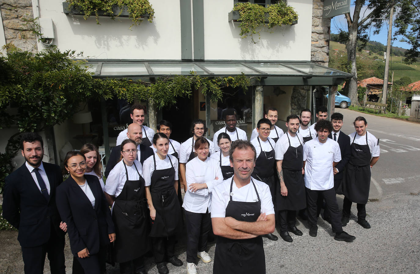 Imagen principal -  Arriba, Nacho celebra los 30 años de Casa Marcial con el personal de sala y cocina y con su hermana Esther y su sobrino Chus. Abajo, el chef ultima un servicio en la cocina de su restaurante. 