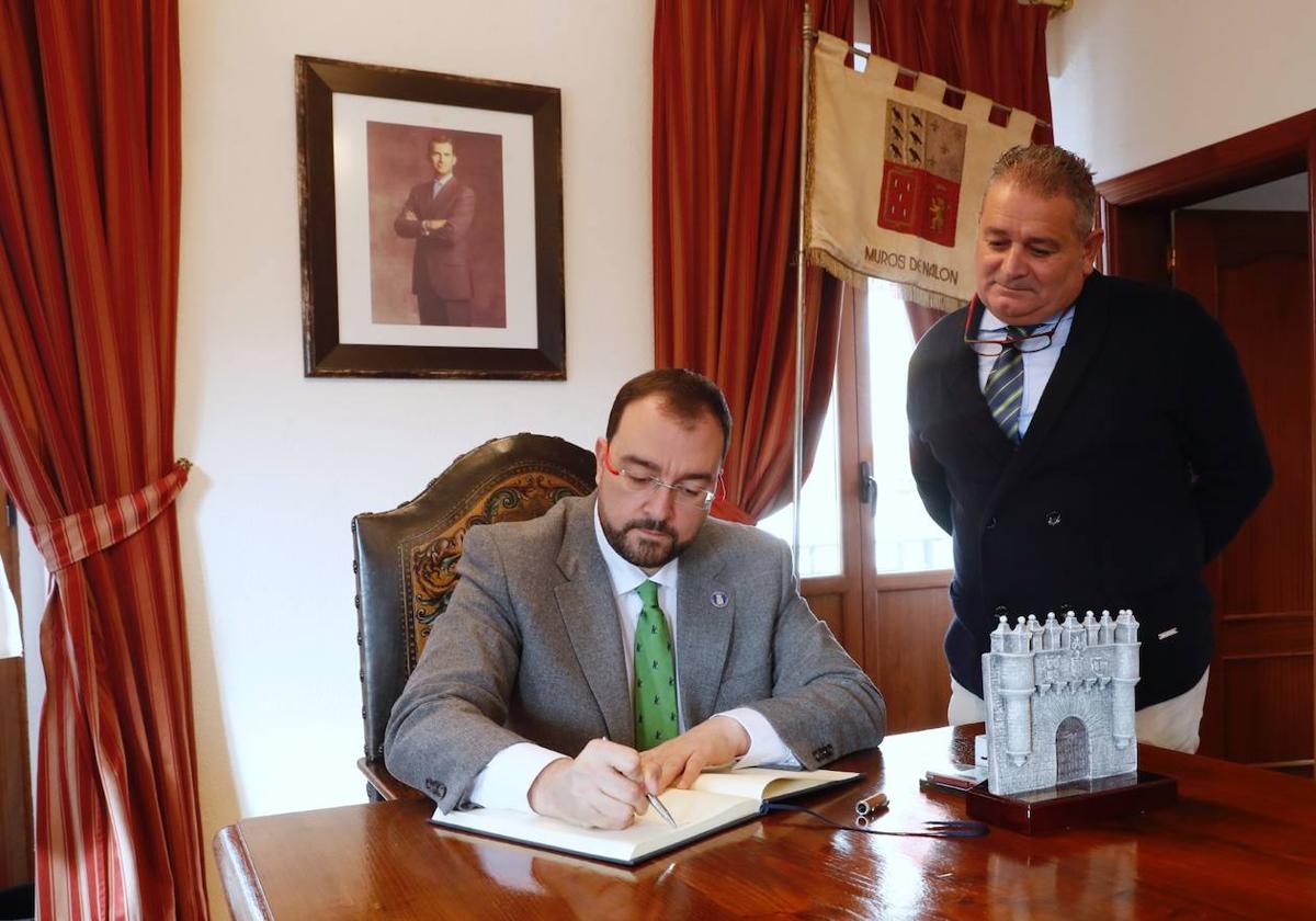 El presidente del Principado, Adrián Barbón, firma en el libro de honor de Muros de Nalón, acompañado por el alcalde del concejo, Celestino Novo.