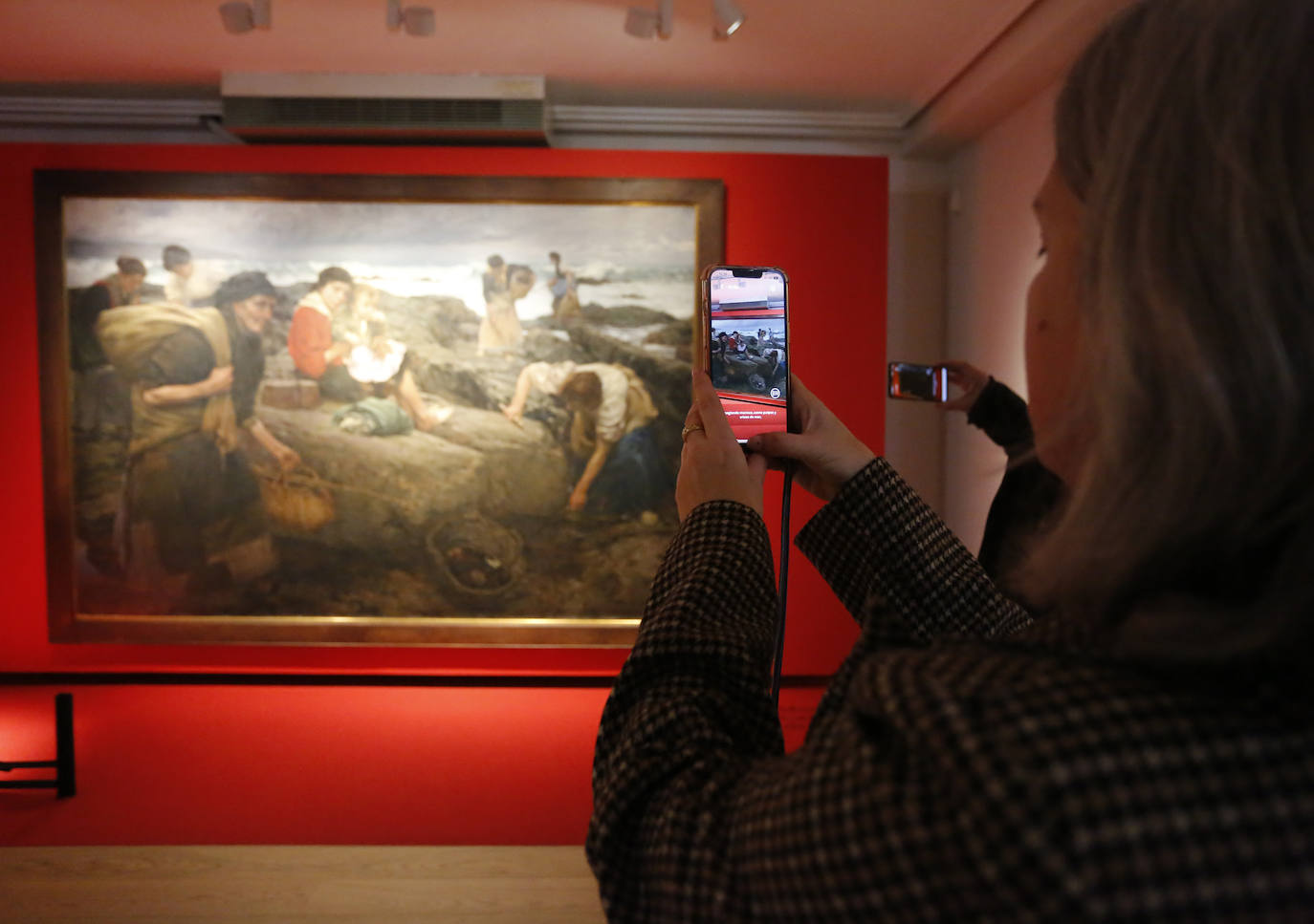 Una persona observa 'Pescadoras de marisco', de Ventura Álvarez Sala, en directo y en el móvil. 