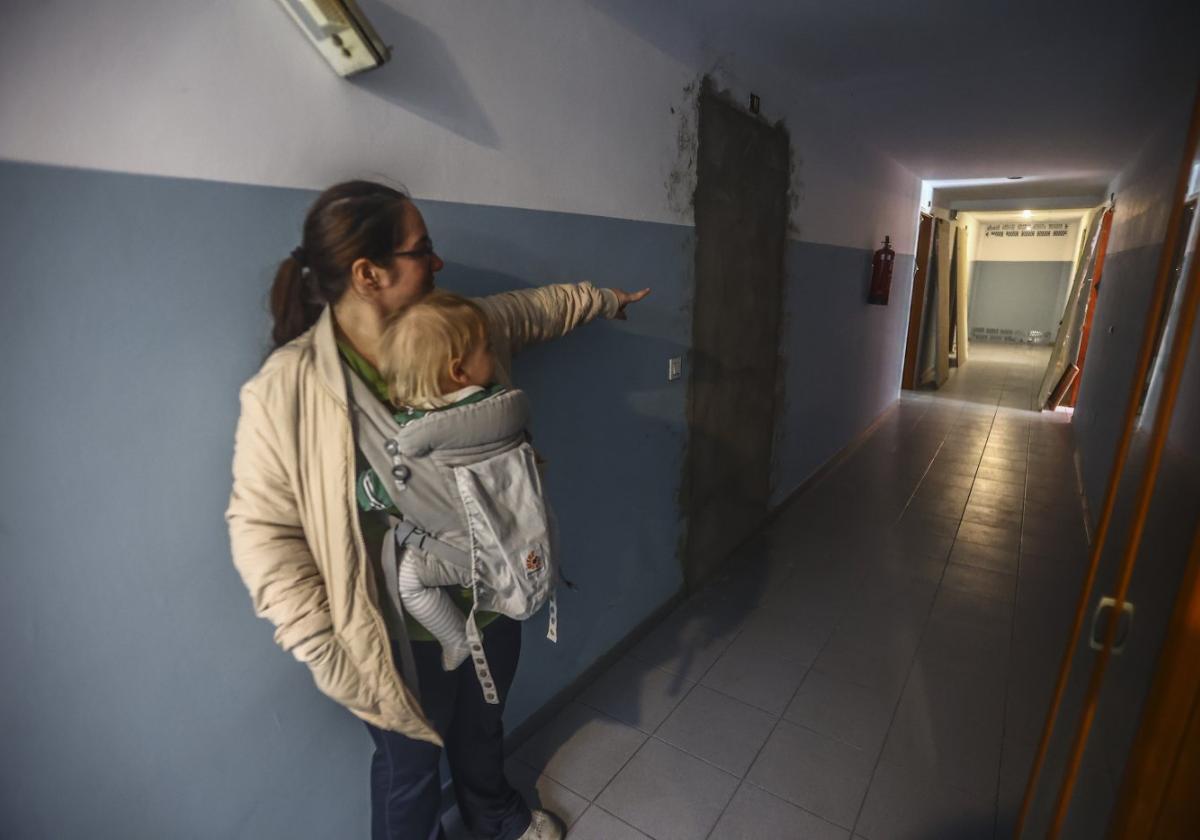 Suyen Álvarez, con su bebé, señala los desperfectos del edificio viviendas sociales de San Roque de Anieves.