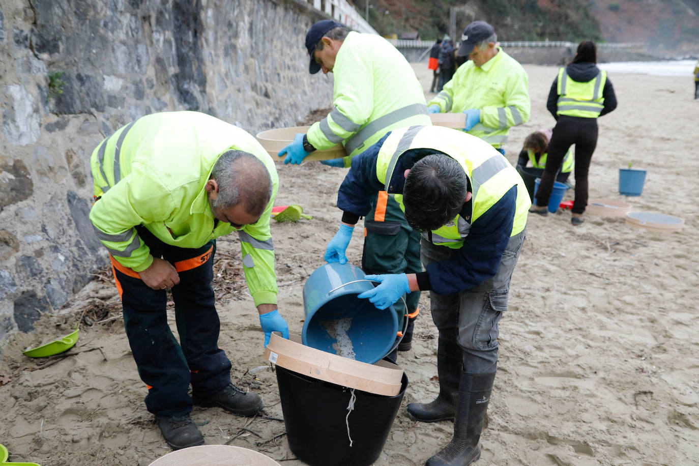 Operarios retiran los pellets o bolitas para fabricar plástico que aparecen en las playas de Asturias, tras la caída de un contenedor de un barco el pasado diciembre, esta mañana en la playa asturiana del Aguilar.