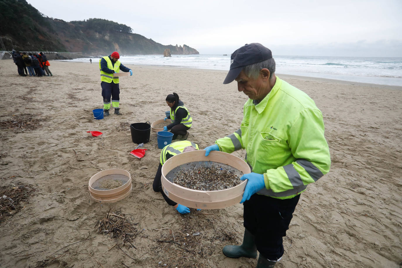 Operarios retiran los pellets o bolitas para fabricar plástico que aparecen en las playas de Asturias, tras la caída de un contenedor de un barco el pasado diciembre, esta mañana en la playa asturiana del Aguilar.