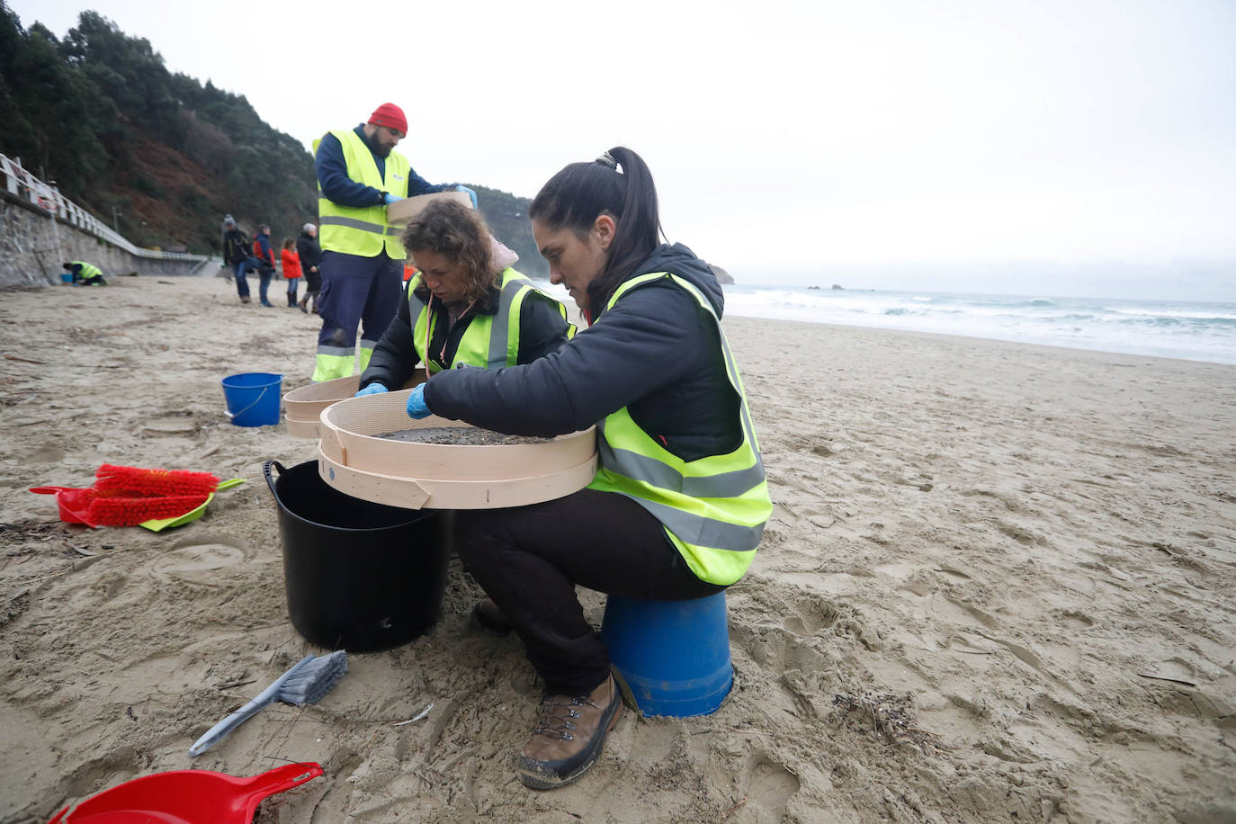 Operarios retiran los pellets o bolitas para fabricar plástico que aparecen en las playas de Asturias, tras la caída de un contenedor de un barco el pasado diciembre, esta mañana en la playa asturiana del Aguilar.