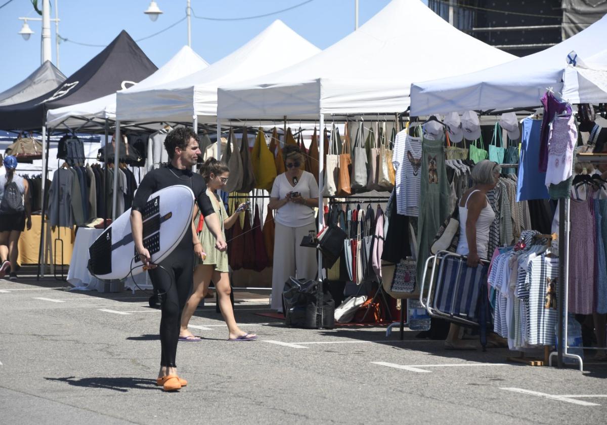 Un surfista pasa delante del mercadillo del Longboard este verano.