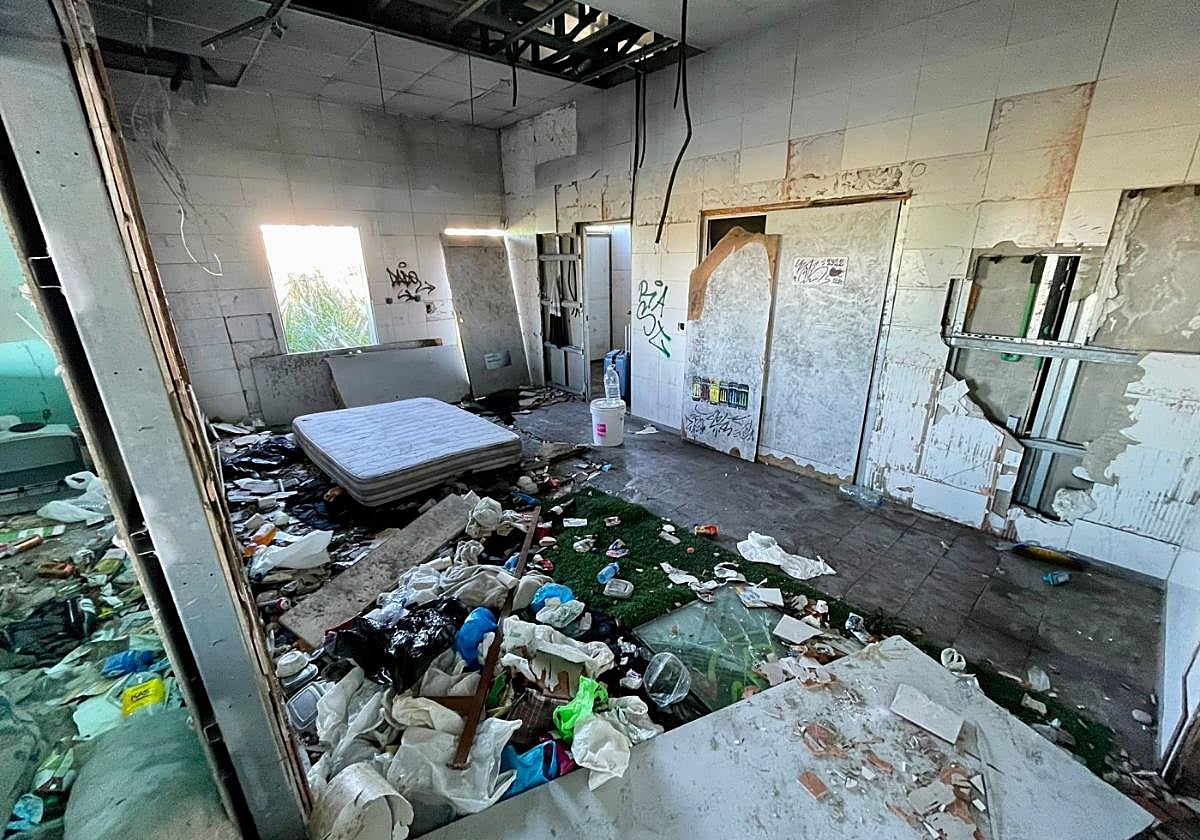 Envases, restos de comida y bolsas de basura alrededor de un colchón en el interior del edificio principal del antiguo complejo deportivo.