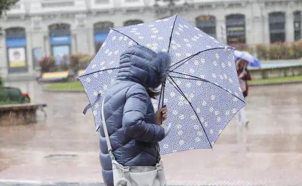 Una mujer se protege de la lluvia y el viento en una calle de Oviedo