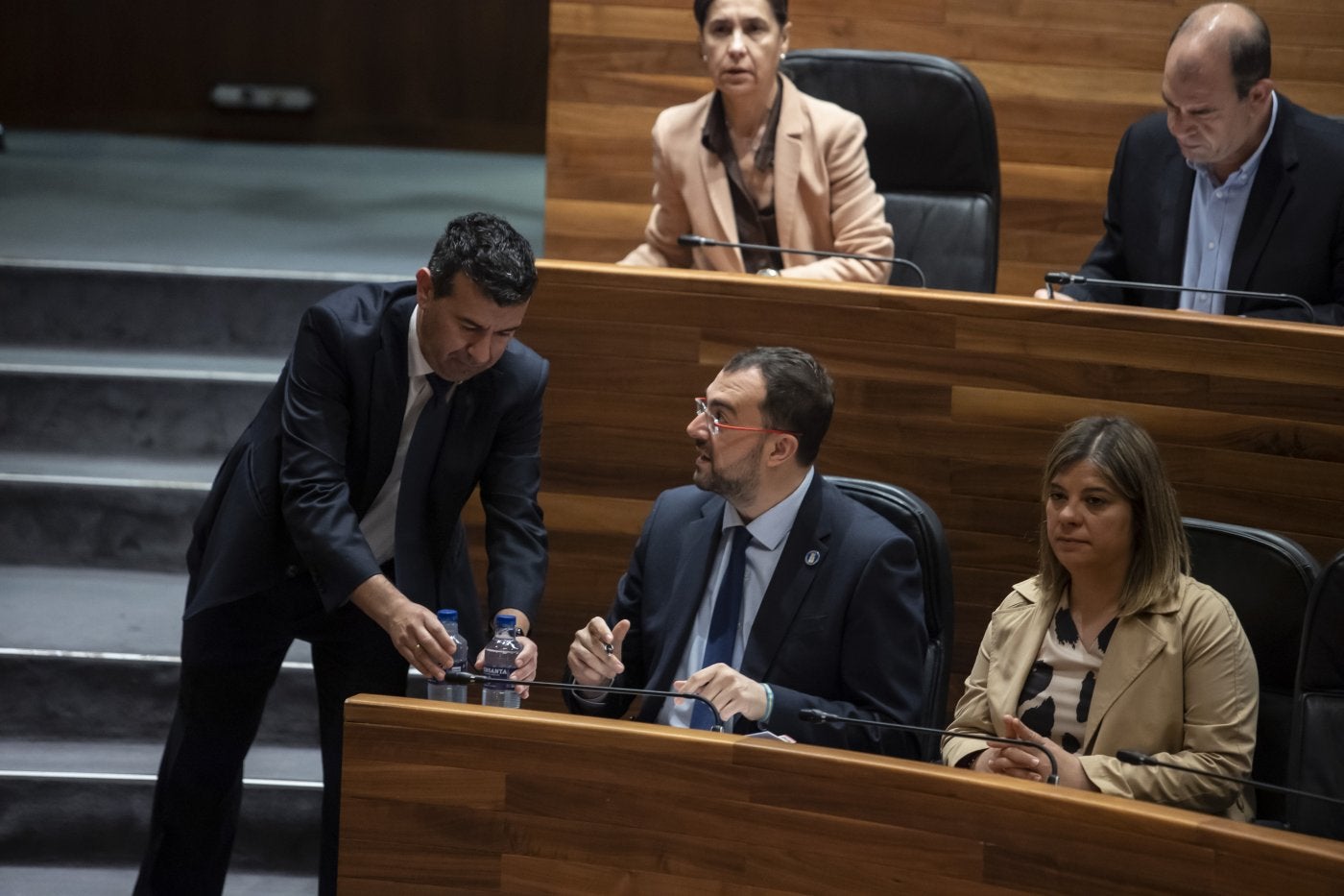Uno de los ujieres de la Junta coloca una botella de agua en el escaño de Barbón.