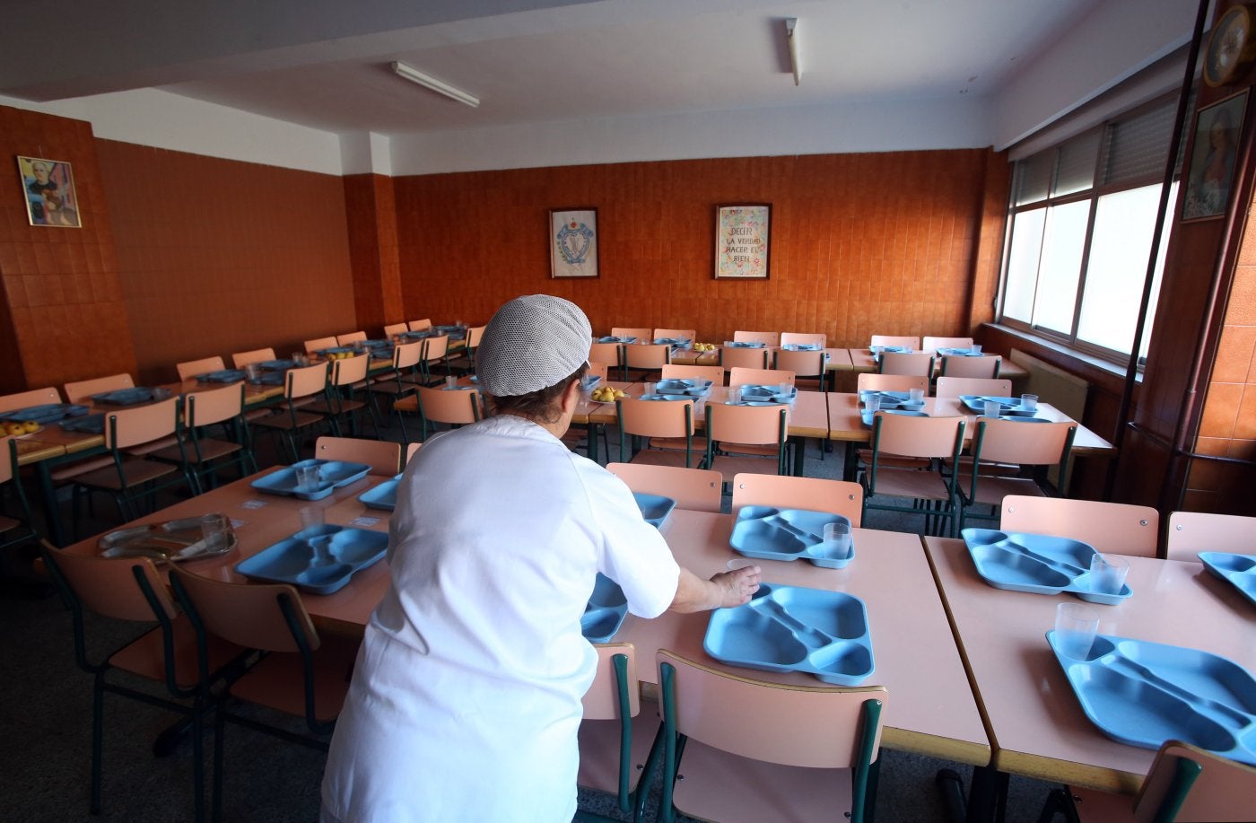 Una empleada preparando las mesas para comer en un colegio.
