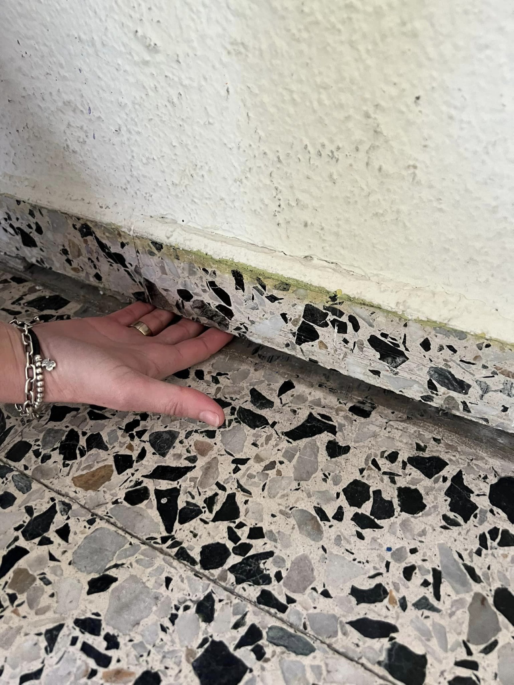 Una de las madres mete la mano en la separación que hay entre la pared y el suelo.