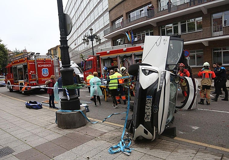 En primer término, el estado en el que quedó el coche siniestrado. Detrás del vehículo, bomberos, policía y sanitarios en el lugar del accidente.