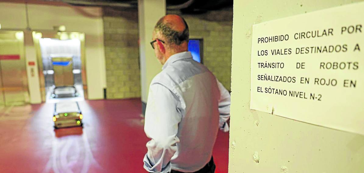 Imagen secundaria 1 - La cocina. Una instalación de 1.500 metros cuadrados en la que trabajan 160 personas. En la imagen, el turno de comida sirve las bandejas en cadena, siguiendo las indicaciones dietéticas pautadas para cada paciente. Los robots. Son 14. Éste, en concreto, espera para acoplarse bajo un carro de comida, ante la mirada de Alfonso Álvarez. Taller. Todos los días se desmonta un robot para hacerle mantenimiento. Como un coche de F1. Al frente del taller está Antolín Eloy Llamas