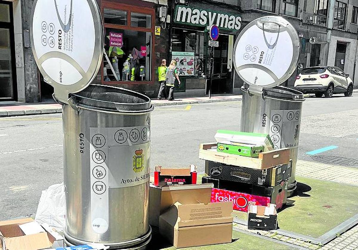 Contenedores de basura con cartones tirado en el suelo en La Pola.