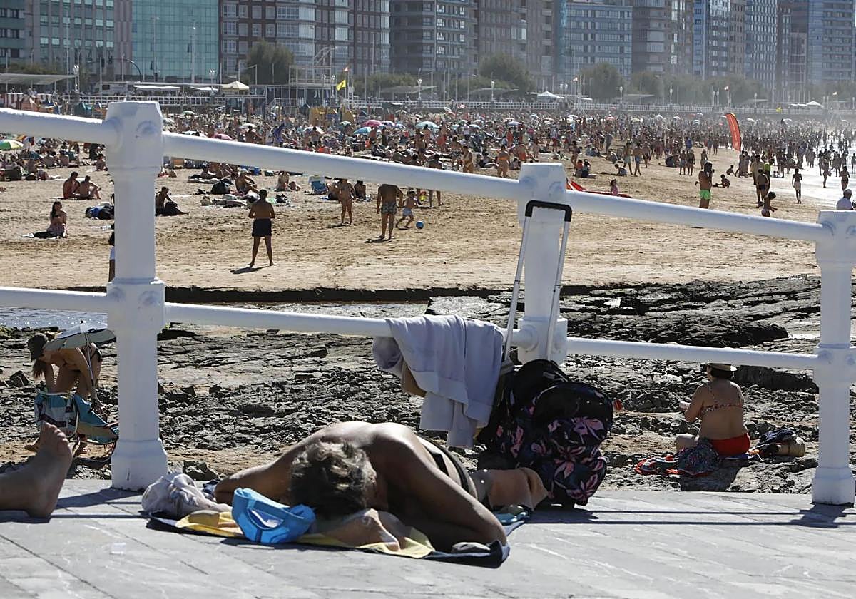 Un hombre toma el sol en la zona asfaltada del entorno de la playa de San Lorenzo.
