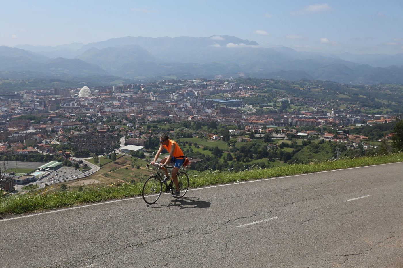 Un ciclista sube al Naranco con el paisaje de la ciudad de Oviedo como telón de fondo.